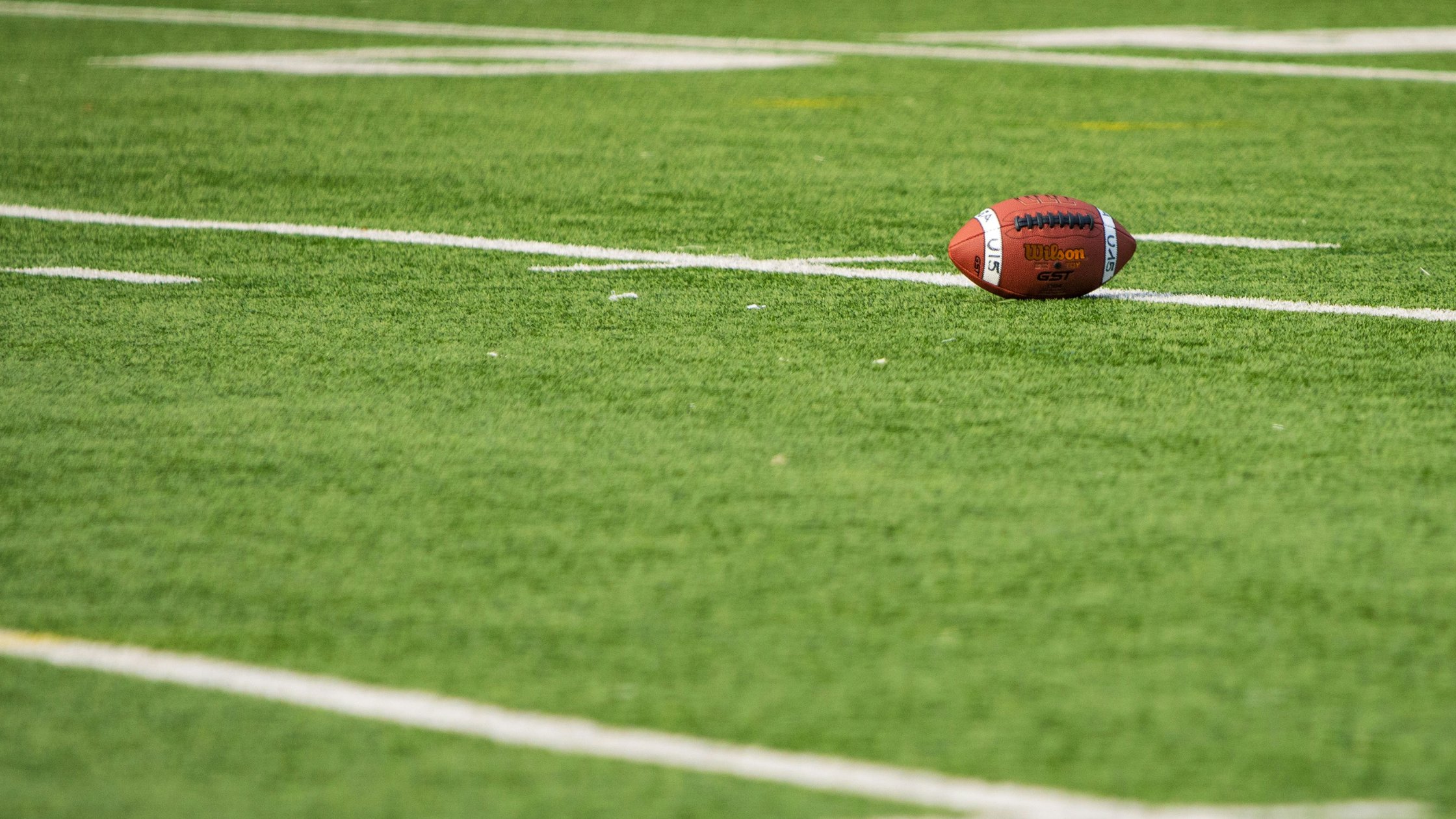 A football resting on a green football field with yard lines in the background.